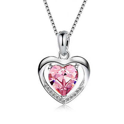 A silver heart pendant necklace featuring a faceted pink heart-shaped crystal in the center, surrounded by a silver heart outline with small clear stones, suspended from a silver box chain on a white background.